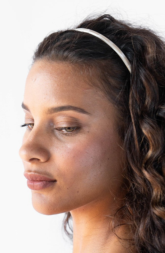 France Luxe marbled ivory white headband for women pictured holding curly, brown hair in a loose hairstyle.