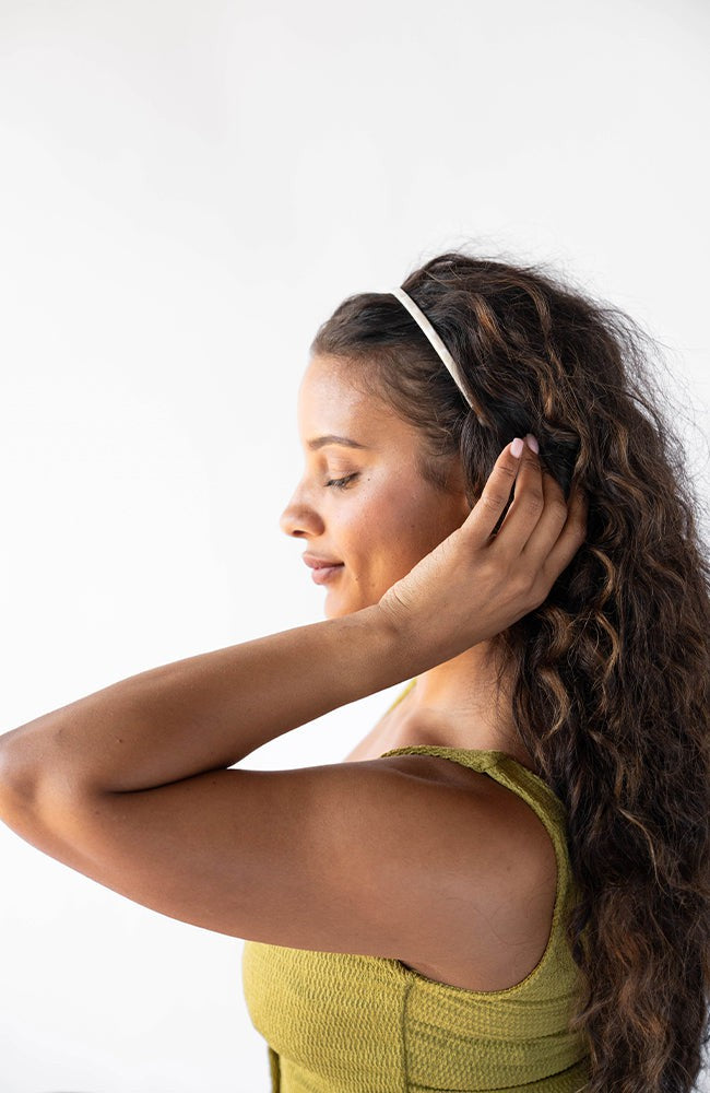 France Luxe marbled ivory white headband for women pictured holding curly, brown hair in a loose hairstyle.
