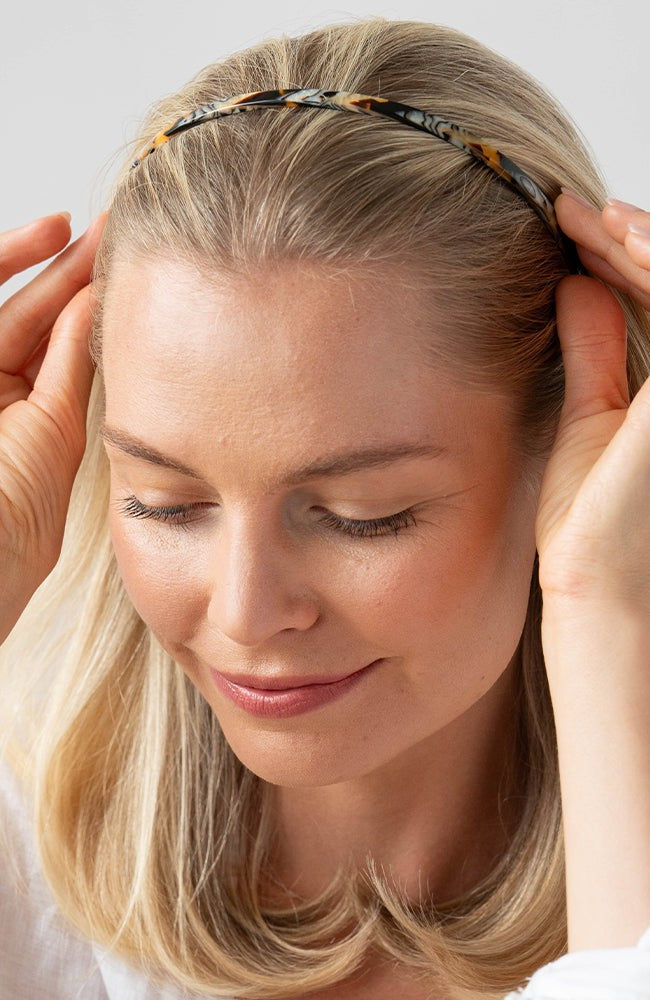 France Luxe thin headband in a golden sand and rich brown color, pictured holding straight, blonde hair in a loose hairstyle.