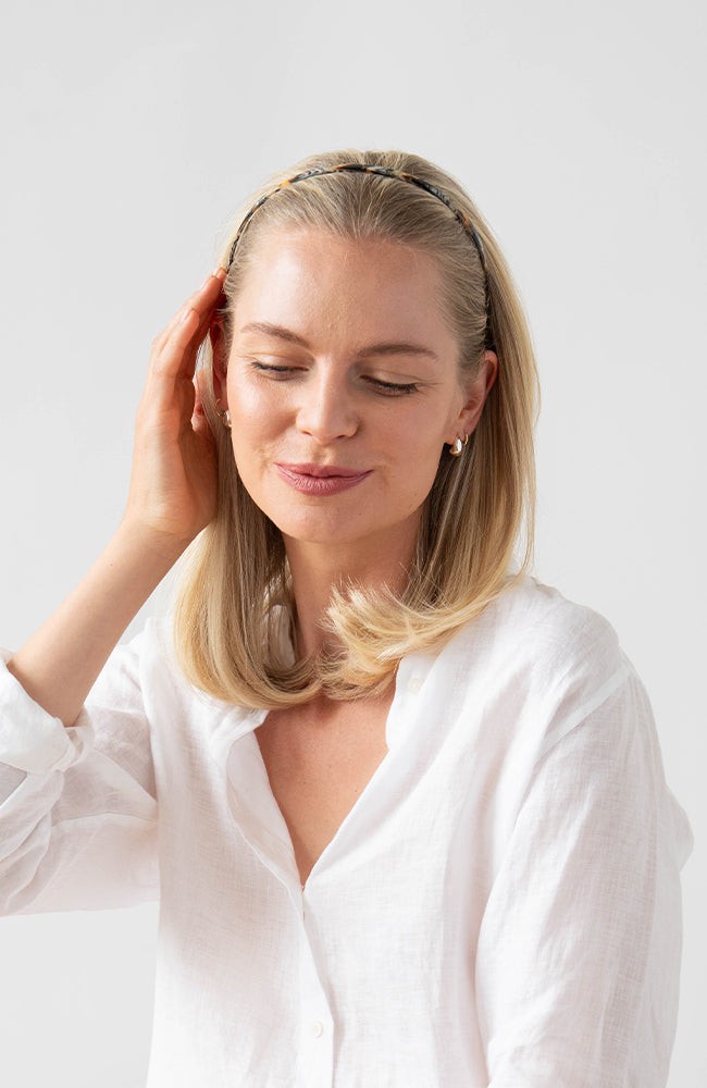 France Luxe thin headband in a golden sand and rich brown color, pictured holding straight, blonde hair in a loose hairstyle.