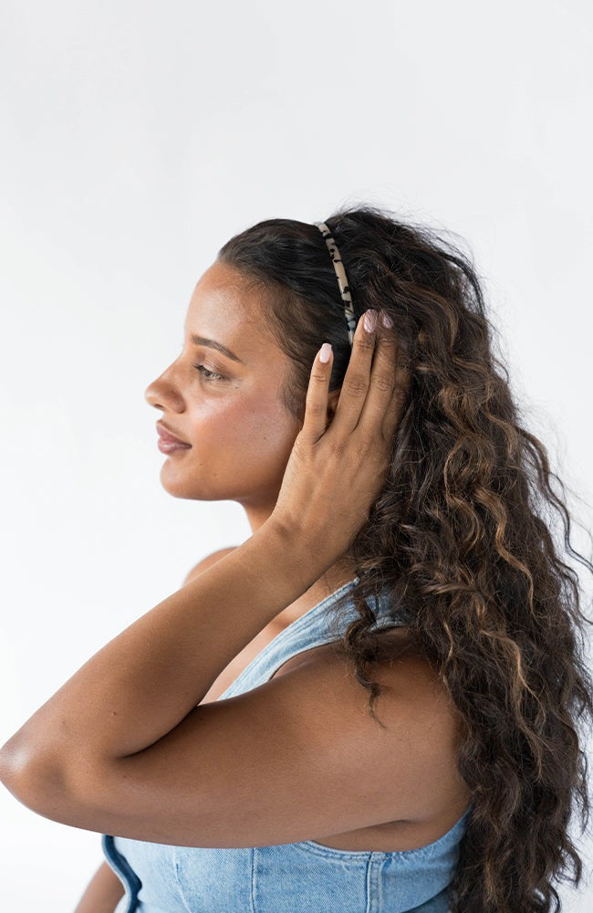 France Luxe thin headband in a Ivory Tortoise Shell color, pictured holding curly, brown hair in a loose hairstyle.
