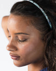 France Luxe thin headband in a light blue, faux shell color, pictured holding curly, brown hair in a loose hairstyle.