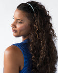 France Luxe thin headband in a light blue, faux shell color, pictured holding curly, brown hair in a loose hairstyle.