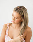 France Luxe thin headband in a textured bronze and amber color, pictured holding straight, blonde hair in a loose hairstyle.