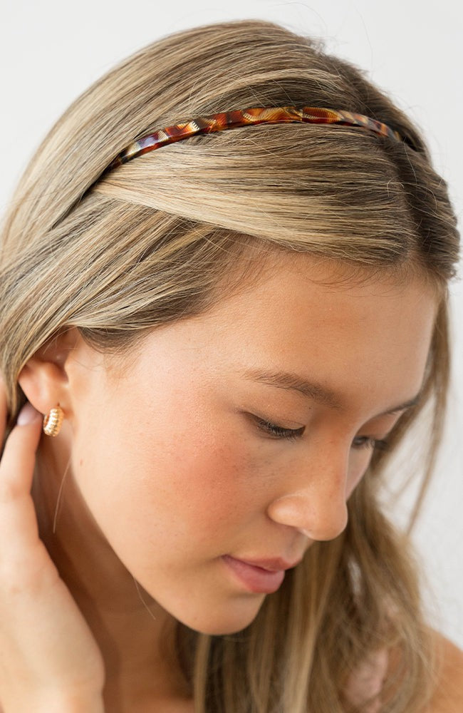 France Luxe thin headband in a textured bronze and amber color, pictured holding straight, blonde hair in a loose hairstyle.