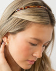 France Luxe thin headband in a textured bronze and amber color, pictured holding straight, blonde hair in a loose hairstyle.