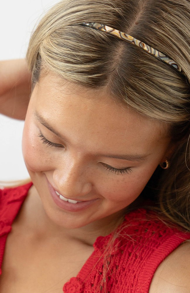 France Luxe thin headband in a marbled gray and charcoal color, pictured holding straight, blonde hair in a loose hairstyle.