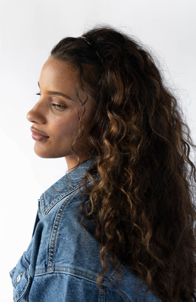 France Luxe thin headband in a metallic burnt sienna and deep chestnut color, pictured holding curly, brown hair in a loose hairstyle.