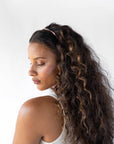France Luxe thin headband in a warm caramel and amber color, pictured holding curly, brown hair in a loose hairstyle.