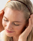 France Luxe thin headband in a rich amber and mahogany brown color, pictured holding straight, blonde hair in a loose hairstyle.
