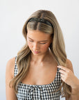 France Luxe marbled pearlescent black headband for women pictured holding straight, blonde hair in a loose hairstyle.