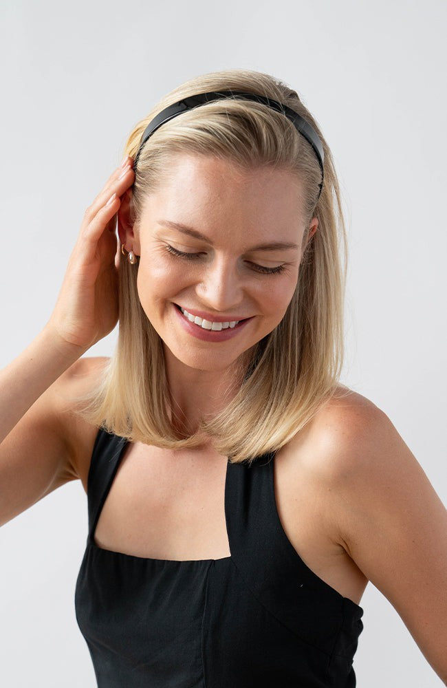 France Luxe classic black headband for women pictured holding straight, blonde hair in a loose hairstyle.