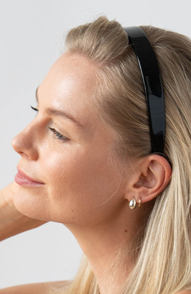 France Luxe classic black headband for women pictured holding straight, blonde hair in a loose hairstyle.