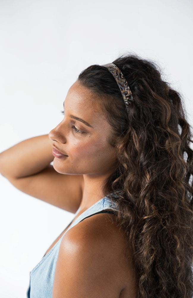 France Luxe wide headband in a marbled gray and charcoal color, pictured holding curly, brown hair in a loose hairstyle.