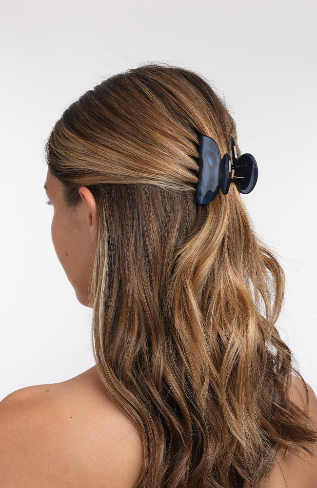 France Luxe small French claw hair clip for women pictured holding wavy, brown hair in a half up hairstyle.