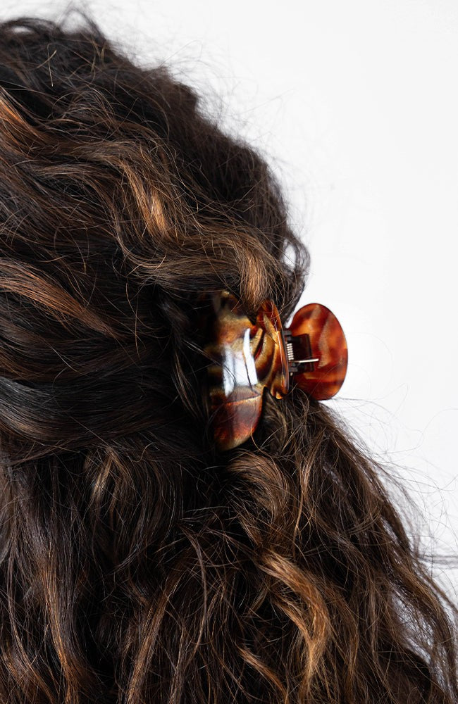 France Luxe small French claw hair clip for women pictured holding curly, brown hair in a half up hairstyle.