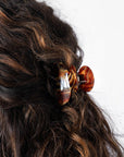 France Luxe small French claw hair clip for women pictured holding curly, brown hair in a half up hairstyle.