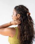 France Luxe small, brown, claw hair clip for women pictured holding curly, brown hair in a half up hairstyle.