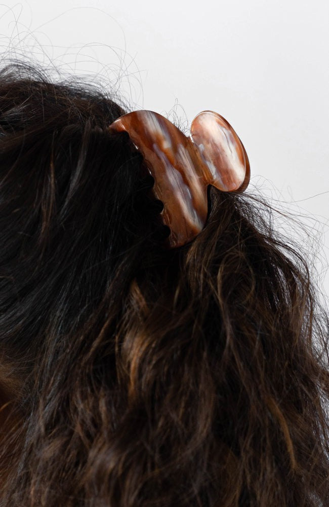 France Luxe small French claw hair clip for women pictured holding curly, brown hair in a half up hairstyle.