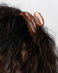 France Luxe small French claw hair clip for women pictured holding curly, brown hair in a half up hairstyle.