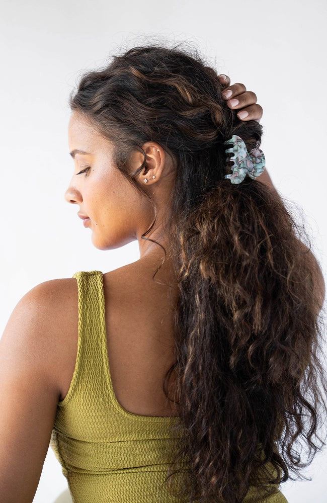 France Luxe small, light blue claw hair clip for women pictured holding curly, brown hair in a half up hairstyle.