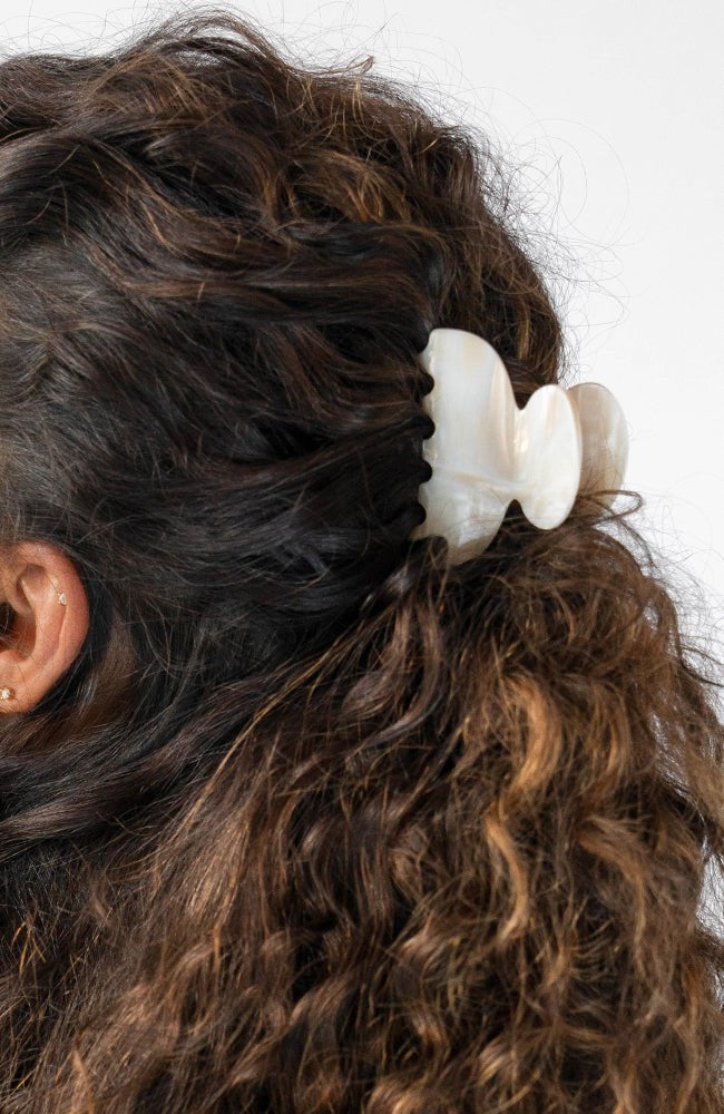 France Luxe small French claw hair clip for women pictured holding curly, brown hair in a half up hairstyle.