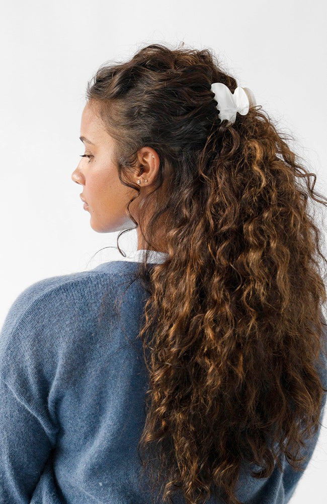France Luxe small, white claw hair clip for women pictured holding curly, brown hair in a half up hairstyle.