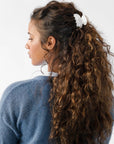 France Luxe small, white claw hair clip for women pictured holding curly, brown hair in a half up hairstyle.