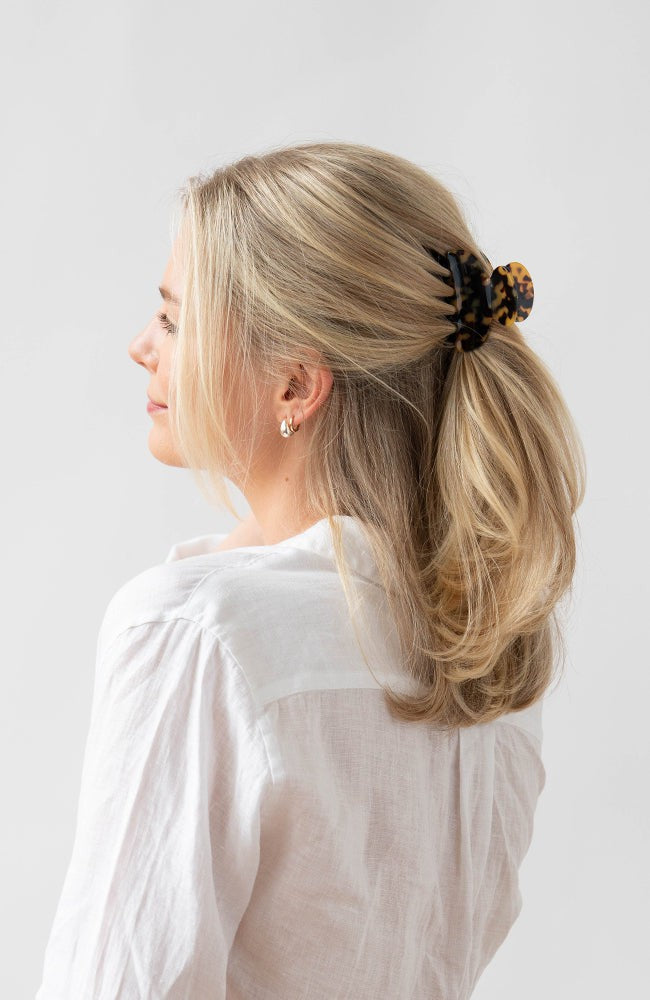 France Luxe small, classic tortoiseshell claw hair clip for women pictured holding straight, blonde hair in a casual half up hairstyle.