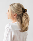 France Luxe small, classic tortoiseshell claw hair clip for women pictured holding straight, blonde hair in a casual half up hairstyle.