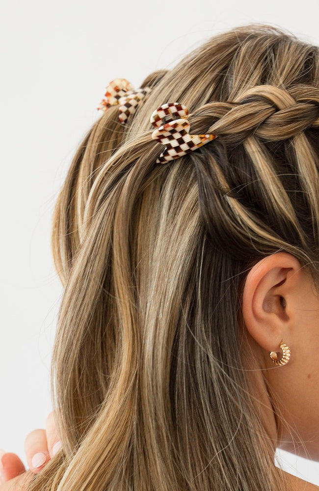 France Luxe mini French claw hair clip for women pictured holding straight, blonde hair in a braided hairstyle.