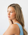 France Luxe mini French claw hair clip for women pictured holding straight, blonde hair in a braided hairstyle.