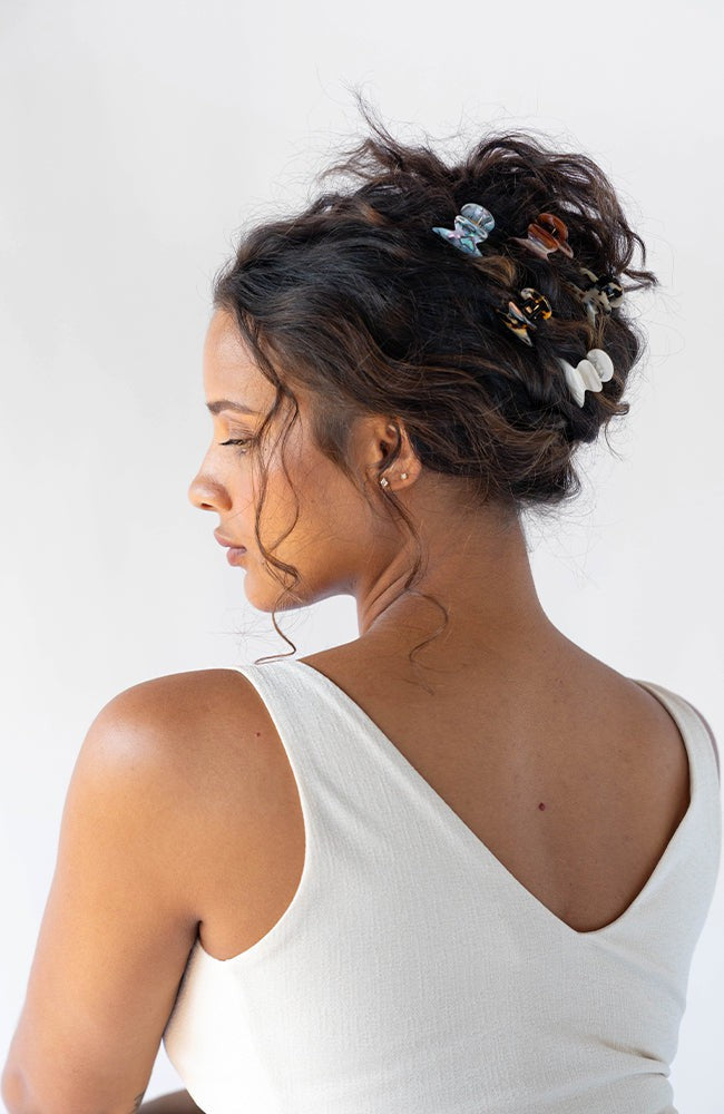 Mini Claw Hair Clip by France Luxe pictured holding curly, brown hair back in a loose bun with multiple different colored hair clips.