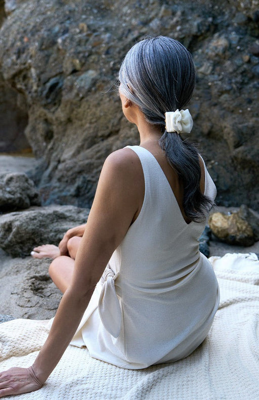 Cream silk covered hair clip holding hair back in a ponytail  at the base of the neck. Woman has beautiful silver and black hair, and sits on the sand.
