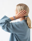 Woman with blonde, straight hair styled in a low ponytail using Blue & Gold, thick hair ties.