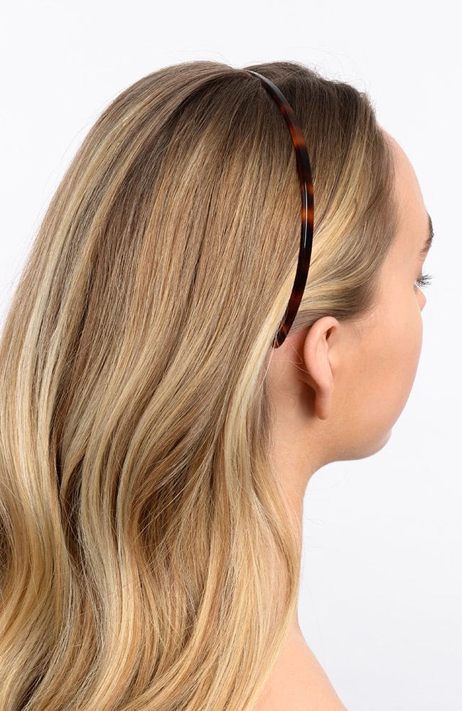 France Luxe thin headband in a Tortoise Shell color, pictured holding straight, blonde hair in a loose hairstyle.