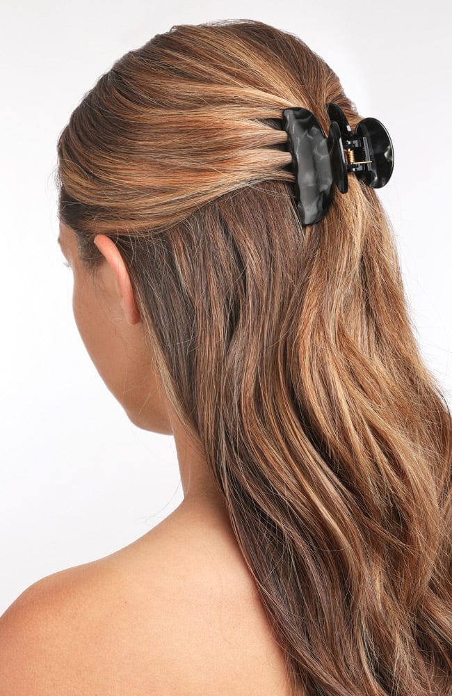 France Luxe small, black claw hair clip for women pictured holding straight, brown hair in a casual half up hairstyle.